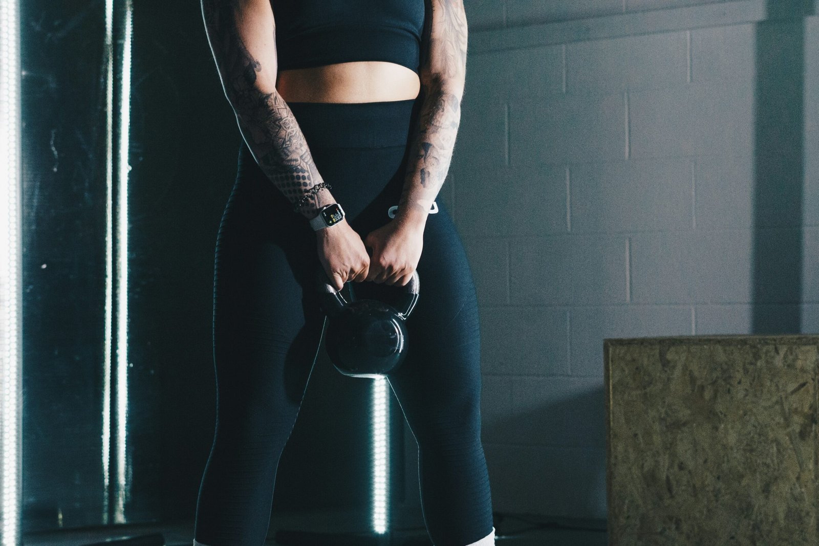 a woman with tattoos holding a kettle in a gym